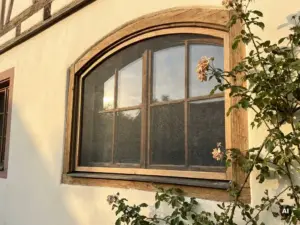 Maßgefertigtes Insektenschutzgitter in einem Bogenfenster einer deutschen Hausfassade mit cremefarbenem Putz im Nachmittagslicht.